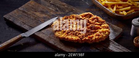 Leckere Pommes frites hinter gebratenem Schnitzel und Messer auf Holz Brett im Café Stockfoto