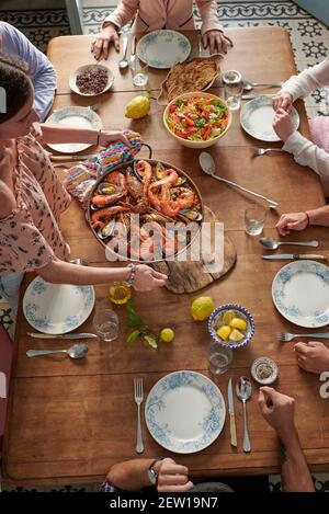 Eine Frau, die Paella mit Meeresfrüchten auf dem Tisch serviert Während des Treffens mit nicht erkennbaren Ernte Freunde im Restaurant Stockfoto