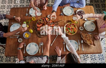 Von oben der Ernte unkenntlich Gruppe von Freunden versammeln sich bei Tisch mit verschiedenen Speisen im spanischen Restaurant und klirrenden Gläsern Mit Getränken während Stockfoto