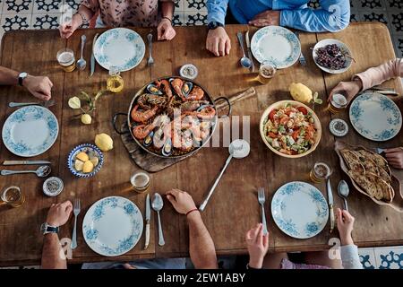 Von oben der Ernte anonyme Gruppe von Freunden versammeln sich bei Serviert Tisch mit Seafood Paella Gericht und verschiedene Speisen während Genießen Sie das Wochenende zusammen in r Stockfoto