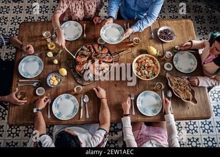 Hoher Winkel der Ernte unkenntlich Gesellschaft von Freunden sitzen herum Holztisch mit verschiedenen Speisen im spanischen Restaurant und genießen Wochenende zusammen Stockfoto