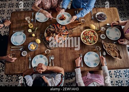 Von oben der Ernte gesichtslose Gesellschaft von Freunden sitzen bei Tisch mit traditioneller Paella mit Meeresfrüchten während des Wochenendes zusammen in Spanisches Restaurant Stockfoto
