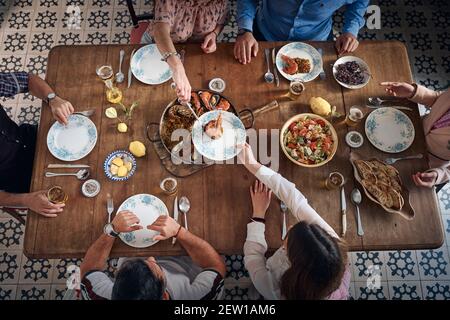 Oben der anonymen Gesellschaft der Freunde, die am Tisch sitzen Und serviert leckere Paella mit Meeresfrüchten auf dem Teller während des Treffens Restaurant Stockfoto