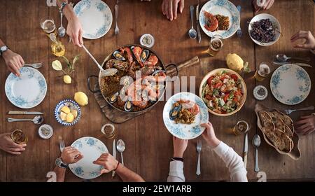 Draufsicht auf Ernte gesichtslose Gruppe von Freunden versammeln sich an Holztisch mit verschiedenen Speisen im spanischen Restaurant Stockfoto