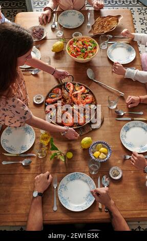 Von oben der Gesellschaft der nicht erkennbaren Freunde, die am Tisch sitzen Mit leckeren Paella Gericht und verbringen Zeit zusammen im Restaurant Stockfoto