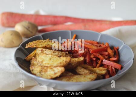 Sautierte Karotten und luftgebratene Kartoffelkeile. Der einfachste und gesunde Weg, um Karotten. Aufnahme auf weißem Hintergrund Stockfoto