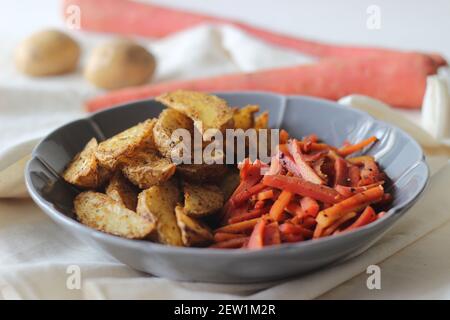 Sautierte Karotten und luftgebratene Kartoffelkeile. Der einfachste und gesunde Weg, um Karotten. Aufnahme auf weißem Hintergrund Stockfoto