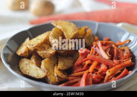 Sautierte Karotten und luftgebratene Kartoffelkeile. Der einfachste und gesunde Weg, um Karotten. Aufnahme auf weißem Hintergrund Stockfoto