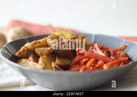 Sautierte Karotten und luftgebratene Kartoffelkeile. Der einfachste und gesunde Weg, um Karotten. Aufnahme auf weißem Hintergrund Stockfoto