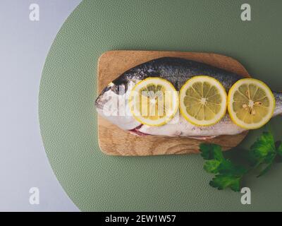 Frisch gebackene dorado oder Seebrasse bereit zum Kochen. Roher Fisch mit Zutaten und Gewürzen wie Zitrone und Petersilie auf der Oberseite. Grüner Hintergrund. Kochen foo Stockfoto