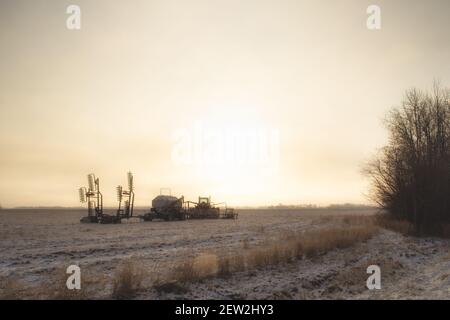 Ein Traktor und Luftsämaschine in einem Schnee geparkt entstaubt Feld unter der Morgensonne in einer ländlichen Agrarlandschaft Stockfoto