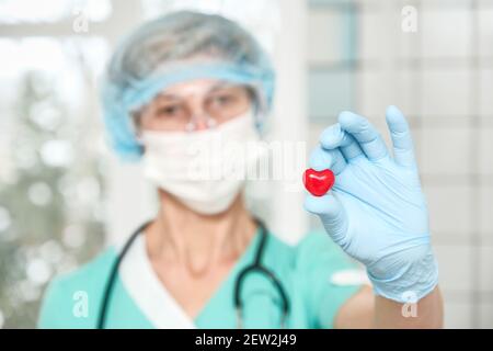 Kardiologe hält rotes Herz im Schutzhandschuh Stockfoto