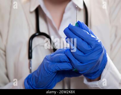 Die blauen Hände des Arztes halten eine Spritze mit einer Nadel fest. Stockfoto