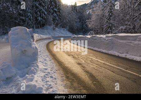 Fahrt auf einer verschneiten Winterstraße durch einen Wald in der Natur mit Sonne scheint. Stockfoto