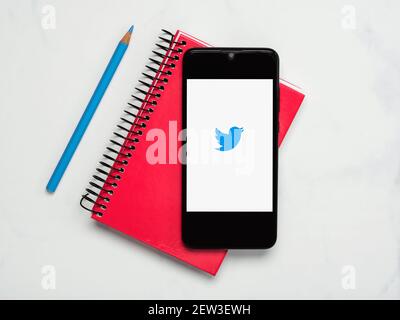 Twitter-Anwendungssymbol auf weißem Bildschirm des Smartphones mit Notebook Und blauer Bleistift auf weißem Hintergrund Stockfoto