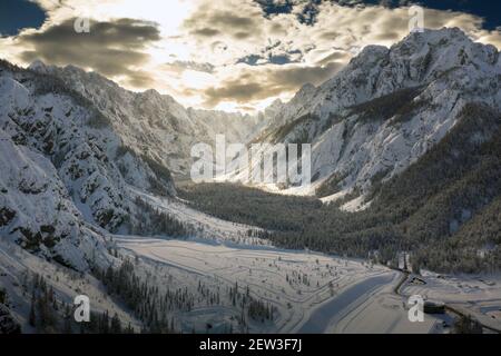 Luftflug über das Bergtal im Winter mit Schnee bedeckt. Filmische Drohnenansicht mit Sonnenlicht, das durch Wolken bricht. Stockfoto