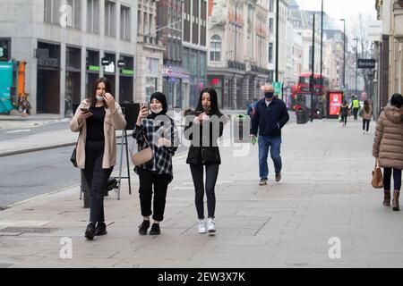 Oxford Street London, während der Coronavirus Covid-19 Pandemic Lockdown Fußgänger in ruhigen Straßen tragen ppe-Masken Blick auf Mobiltelefone, wie sie in ungewöhnlich leeren Straße gehen Stockfoto