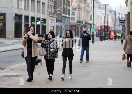 Oxford Street London, während der Coronavirus Covid-19 Pandemic Lockdown Fußgänger in ruhigen Straßen tragen ppe-Masken Blick auf Mobiltelefone, wie sie in ungewöhnlich leeren Straße gehen Stockfoto