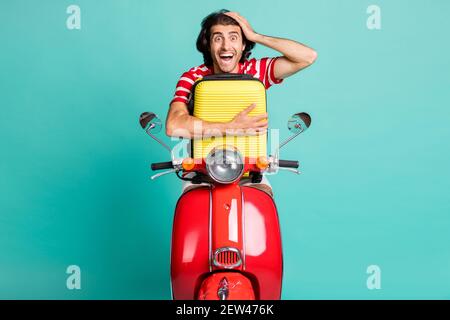 Portrait von gut aussehend erstaunt fröhlichen Kerl Reiten Moped Umarmung Tasche Spaß isoliert über hellgrün türkisfarbenen Hintergrund Stockfoto