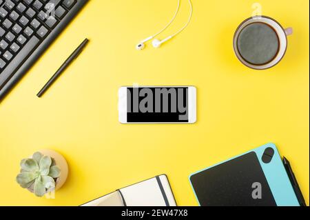 Minimaler Schreibtisch. Flat Lay - Smartphone-Modell, Tastatur, Kopfhörer, Tablet auf gelbem Hintergrund. Draufsicht. Arbeitsplatzkonzept. Für Text platzieren. Stockfoto