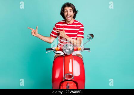 Portrait von schönen erstaunt fröhlich Kerl Reiten Moped demonstrieren Kopie Raum isoliert über hellgrünen türkisfarbenen Hintergrund Stockfoto
