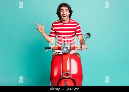 Portrait von gut aussehend fröhlich erstaunt Kerl Reiten Moped zeigt Kopie Raum isoliert über hellgrünen türkisfarbenen Hintergrund Stockfoto