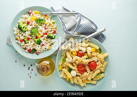 Frischer Nudelsalat und Reissalat mit gemischtem Gemüse in Tellern auf blauem Hintergrund. Gesunde Pasta und Reisgerichte Stockfoto