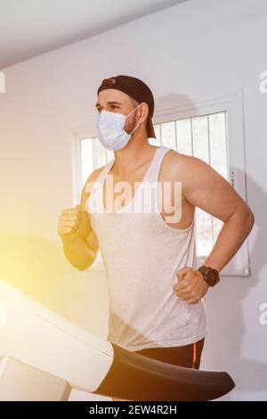 Mann, der auf einem Laufband läuft und eine Maske trägt. Covid19. Gesundheits- und Sicherheitskonzept. Stockfoto