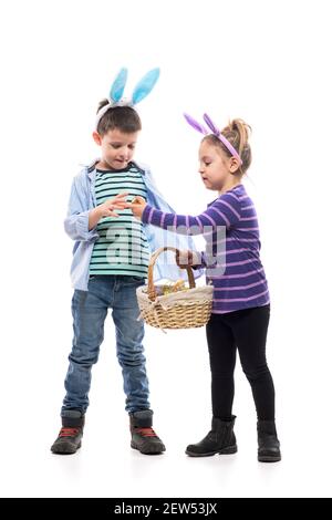 Spielerisch neugierig interessierten kleinen Kindern Jungen und Mädchen spielen mit Ostereier halten Korb. Ganzkörper isoliert auf weißem Hintergrund. Stockfoto