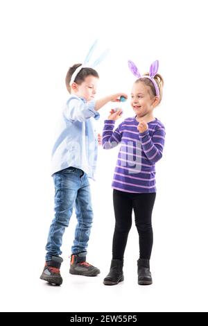 Spielerische junge Geschwister Kinder spielen Osterei knacken Kampf. Ganzkörper isoliert auf weißem Hintergrund. Stockfoto