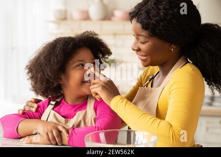 Liebevolle Schwarze Mutter Spielt Mit Ihrer Tochter, Während Sie Backen In Der Küche Stockfoto