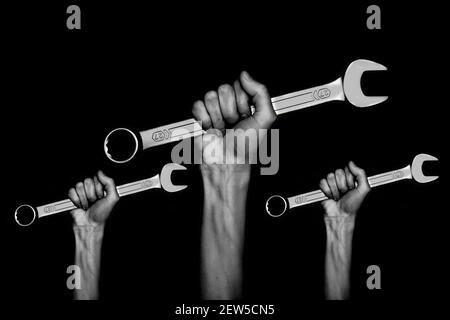 Schwarz-Weiß-Foto. Drei Schraubenschlüssel in den Händen der Frauen. Hände hält einen Schraubenschlüssel auf einem grauen Hintergrund. Kombinationsschlüssel. Großer Chrom-Vanadium-spann Stockfoto