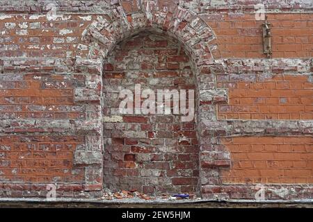 Zerstörte gemauerte Fenster Öffnung auf einer roten Ziegelmauer in einem alten verlassenen Haus. Stockfoto