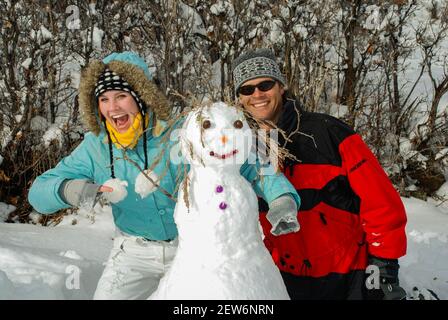 Vater und Erwachsene Tochter haben Spaß buidling ein Schneemann zusammen. Blick auf die Kamera. Stockfoto