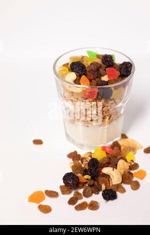 Müsli Dessert im Glas mit Joghurt und kandierten oder getrockneten Früchten mit Himbeeren auf weißem Hintergrund isoliert. Rosinen, Nüsse und kandierte Früchte Stockfoto
