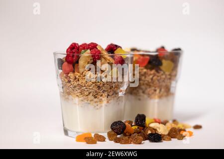 Müsli Dessert im Glas mit Joghurt und kandierten oder getrockneten Früchten mit Himbeeren auf weißem Hintergrund isoliert. Rosinen, Nüsse und kandierte Früchte Stockfoto