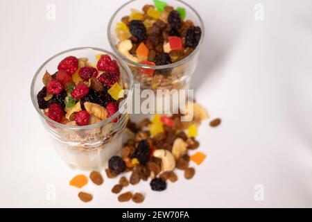 Müsli Dessert im Glas mit Joghurt und kandierten oder getrockneten Früchten mit Himbeeren auf weißem Hintergrund isoliert. Rosinen, Nüsse und kandierte Früchte Stockfoto