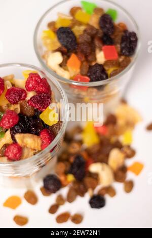 Müsli Dessert im Glas mit Joghurt und kandierten oder getrockneten Früchten mit Himbeeren auf weißem Hintergrund isoliert. Rosinen, Nüsse und kandierte Früchte Stockfoto