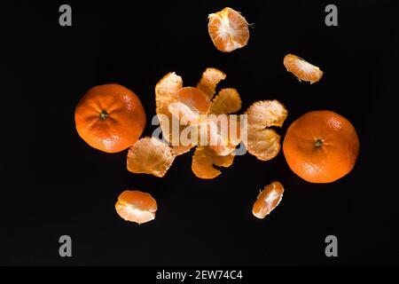 Reife Frucht der Zitruspflanze Mandarine, ganz und Scheiben und mit Schälchen auf schwarzem Hintergrund Stockfoto
