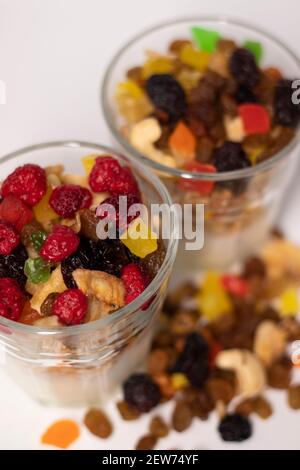 Müsli Dessert im Glas mit Joghurt und kandierten oder getrockneten Früchten mit Himbeeren auf weißem Hintergrund isoliert. Rosinen, Nüsse und kandierte Früchte Stockfoto