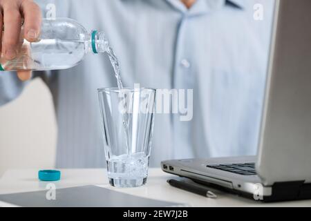 Ein Mann mit Laptop gießt ein Glas Wasser aus einer Flasche. Stockfoto