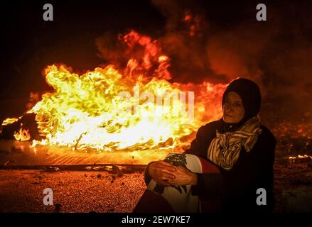 Beirut, Libanon. März 2021, 02nd. Eine alte Frau sitzt vor brennenden Reifen während eines Protests gegen die libanesische Lira-Abwertung gegenüber dem Dollar auf dem Schwarzmarkt aufgrund der sich verschärfenden Wirtschaftskrise des Landes. Quelle: Marwan Naamani/dpa/Alamy Live News Stockfoto