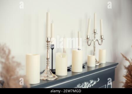 Kerzen verschiedener Typen und Größen mit und ohne Kerzenständer Auf der imitierten Feuerstelle in der Nähe der Wand Stockfoto