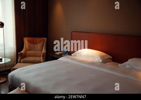 Typisches Hotelzimmer. Das Bett ist mit schneeweißer Bettwäsche, Kissen und Fenster bedeckt Stockfoto