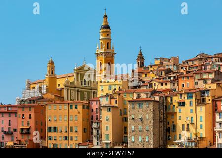 Blick auf bunte Häuser und Glockenturm der Basilika Saint Michel Archange unter blauem Himmel in Menton - kleine Stadt an der französischen Riviera. Stockfoto