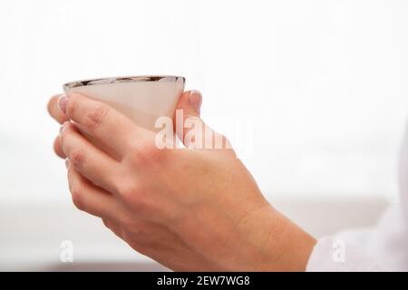 Weibliche Hände mit gepflegter Maniküre halten eine Kaffeetasse hinein Vorderseite des Fensters Stockfoto