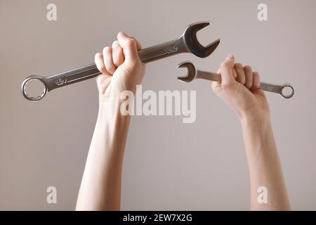 Zwei Schraubenschlüssel in den Händen der Frauen. Hände halten einen Schraubenschlüssel auf einem grauen Hintergrund. Kombinationsschlüssel. Großer Chrom-Vanadium-Schraubenschlüssel in der Hand. Frauen w Stockfoto