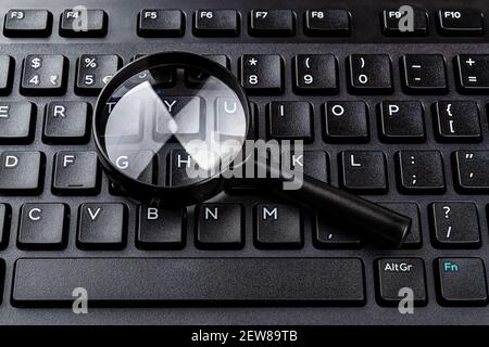 Lupe auf der schwarzen Computertastatur Nahaufnahme. Suche nach Schlüsselwörtern und Online-Ressourcen, Netzwerksuche, Internet-Sicherheitskonzepte. Stockfoto