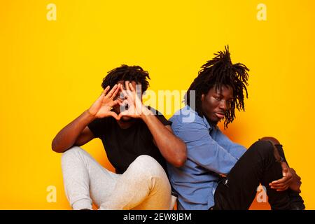 Zwei afroamerikanische Jungs posieren fröhlich zusammen auf gelbem Hintergrund, Lifestyle Menschen Konzept Stockfoto