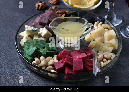 Mehrfarbiger Gourmet-Käse, Oliven, Nüsse, Honig und Zitronenscheiben auf dunklem Hintergrund. Vorspeise für eine Weinparty. Nahaufnahme Stockfoto